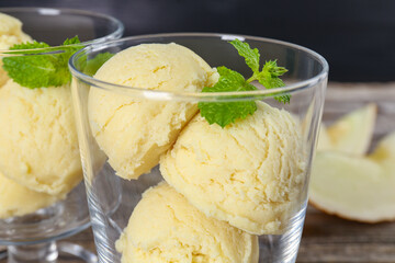 Scoops of melon sorbet and mint in glass dessert bowls on table, closeup
