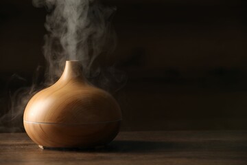 Aroma oil diffuser with steam on wooden table, space for text