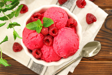 Delicious raspberry sorbet in bowl, fresh berries, mint and spoon on wooden table, flat lay