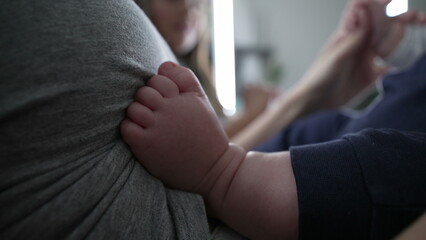 Close-up of baby gripping adult's shirt with feet while being held, focusing on the delicate foot gesture. tender and intimate moment between baby and parent