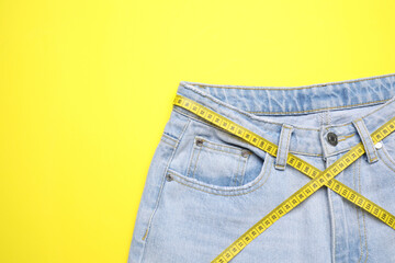 Jeans and measuring tape on yellow background, top view. Space for text