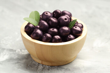 Ripe acai berries and leaves in bowl on grey textured table, closeup