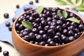 Ripe acai berries and leaves in bowl on grey table, closeup