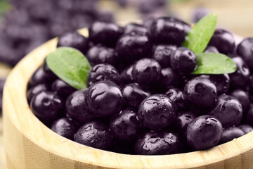 Ripe acai berries and leaves in bowl, closeup