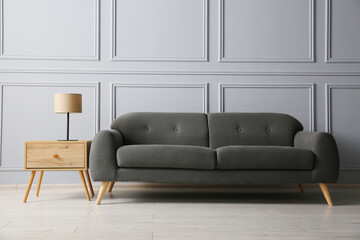 Stylish sofa and lamp on side table near grey wall