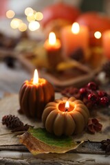 Burning candles in shape of pumpkins, old book and autumn decor on table, closeup