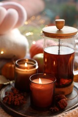 Burning candles, freshly brewed tea and autumn decor on fabric, closeup