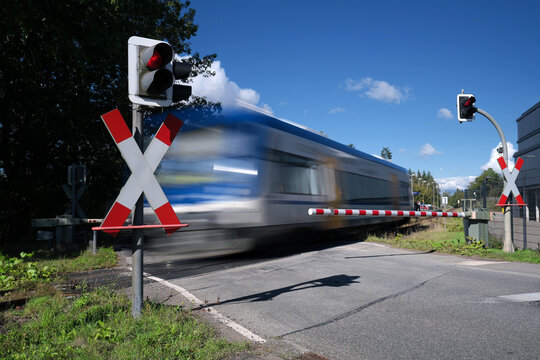 Bahn&uuml;bergang mit Halbschranke und rotem Signal und vorbeifahrendem Triebwagen - Stockfoto