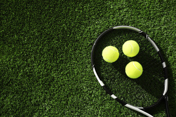 Tennis racket and balls on green artificial grass, flat lay. Space for text