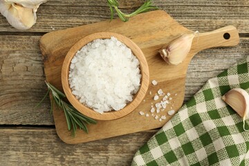 Sea salt in bowl, rosemary and garlic on wooden table, top view