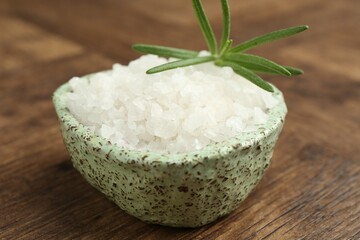 Sea salt and rosemary in bowl on wooden table, closeup