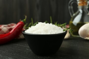 Sea salt and thyme in bowl on dark gray textured table, closeup