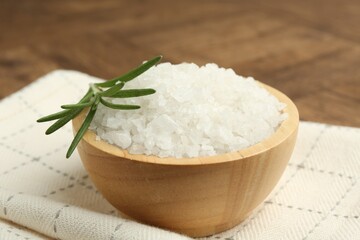 Sea salt and rosemary in bowl on brown table, closeup