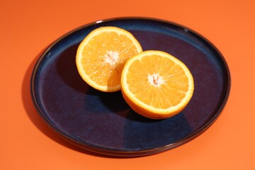 Dark blue plate with orange halves on orange background, closeup