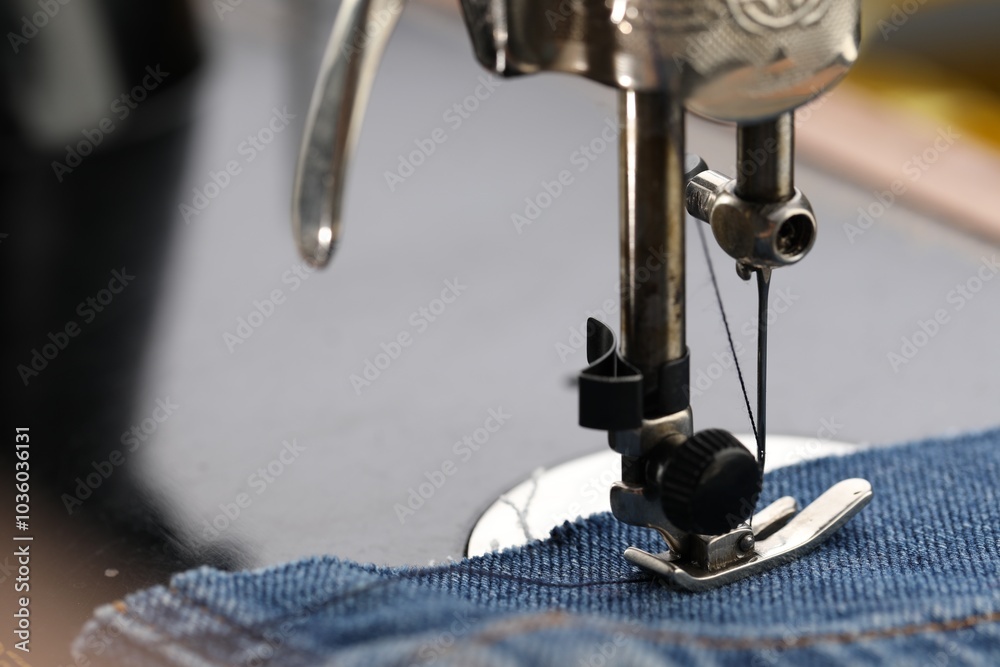 Wall mural Professional sewing machine with denim fabric on blurred background, macro view