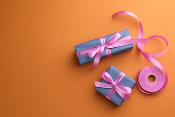 Beautiful gift boxes with pink bows on orange background, top view. Space for text