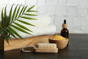 Spa treatment. Towels, sea salt, brush, bottle of serum and palm leaf on black wooden table, closeup
