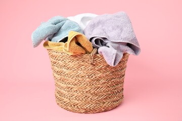 Obraz premium Wicker basket full of laundry on pink background