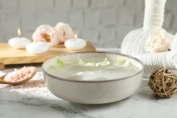 Spa composition with bowl of water and burning candles on white marble table, closeup