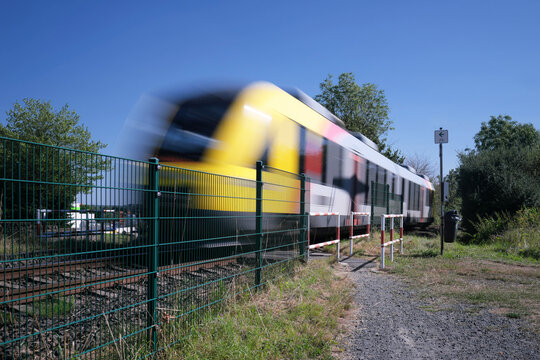 Bahn&uuml;bergang f&uuml;r Fu&szlig;g&auml;nger und Umlaufgitter und Zaun und durchfahrender Zug - Stockfoto