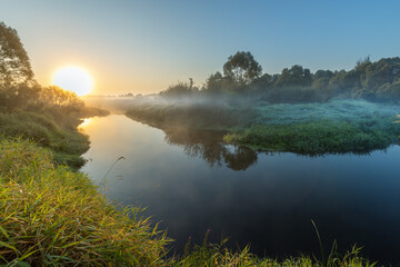 The sun is setting over a river, casting a warm glow on the water