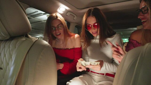 POV Three Joyful girlfriends Split the Fare and Pay the Taxi Driver with Dollar Bills, Laughing and Enjoying Their Ride Together