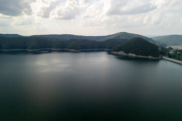 Obraz premium A breathtaking view of a serene lake surrounded by lush green hills and cloudy skies, perfect for nature lovers and outdoor enthusiasts.