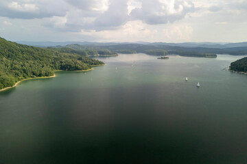 Aerial view of a tranquil lake surrounded by lush green hills and sailboats in the distance, perfect for nature lovers and outdoor enthusiasts.