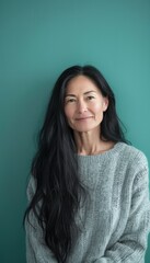 Obraz premium Confident Woman with Long Black Hair in Grey Sweater Against Teal Background