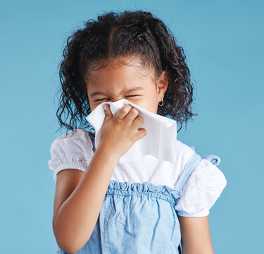 Girl, child and sneeze with tissue in studio, sick or cold with mucus, cleaning nose and hygiene by blue background. Girl, allergies or hay fever with paper towel for infection, virus and bacteria