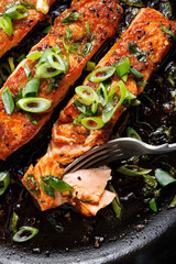 Close-up view of teriyaki salmon sprinkled with chopped scallion in a black baking dish