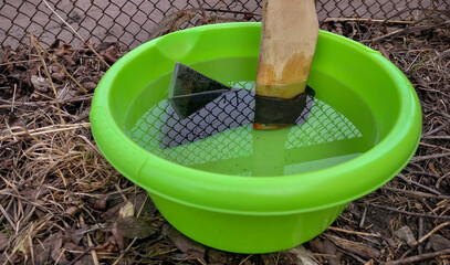 The farmer placed the axe in water poured into a green basin so that the handle would not fly off...