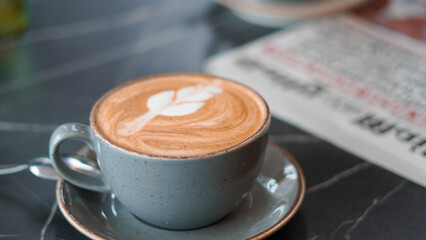 Close-up of a latte with intricate pattern beside a morning newspaper