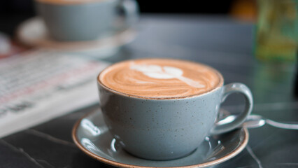 Close-up of a latte with intricate pattern beside a morning newspaper