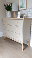 Fototapeta premium A modern white chest of drawers sits against a rustic brick wall, featuring a lamp and a decorative vase on top, creating a chic interior ambiance perfect for any room