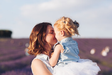 Happy and smiling mother and a little adorable cute blond daughter are hugging and kissing in a lavender field at sunset