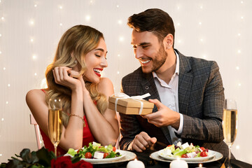 Happy man giving valentine's day present to his surprised girlfriend at romantic dinner in...