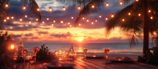 Romantic dinner table set on the beach at sunset with palm trees and string lights.