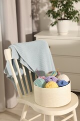 Box with colorful yarns and crochet hooks on chair indoors