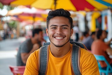 Naklejka premium a happy male hispanic college student having fun with friends sitted on a plastic table with chairs and an umbrella out of a latin american street market, they are dressed casual.