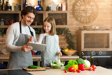 Best Recipe Apps. Cheerful young father and his little daughter using digital tablet in kitchen, choosing what to cook