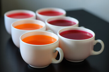 White cups with sweet dessert jelly (orange, cherry and strawberry), placed on a black surface, limited depth of field, selective focus, close-up