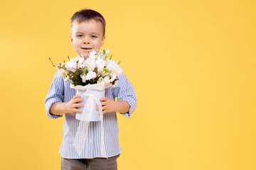 Smiling elegant boy with a bouquet of flowers. Gift for mom. Floral gift. Stylish little boy in holding a bouquet of tulips. Birthday, Women's Day, Mother's Day, Valentine's Day. wedding concept