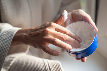 Mature woman is applying a hand cream in bathroom, close-up cropped shot. Morning beauty treatment...