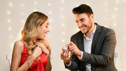 Loving man making proposal to his surprised girlfriend on romantic date in restaurant, presenting engagement ring