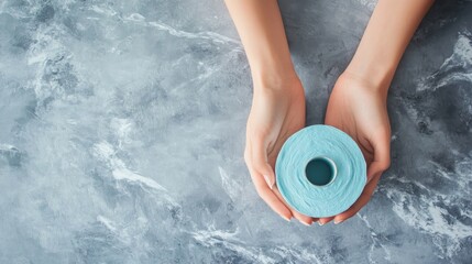 A person holding a light blue spool of thread on a textured gray surface.