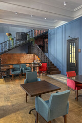 cozy vintage interior of the cafe restaurant with blue walls, wooden floors and brickwork. blue and red chairs are arrenged around tables. natural lighting and lamps.