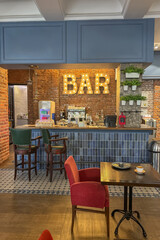cozy vintage interior of the cafe restaurant with blue walls, wooden floors and brickwork. blue and red chairs are arrenged around tables. natural lighting and lamps.