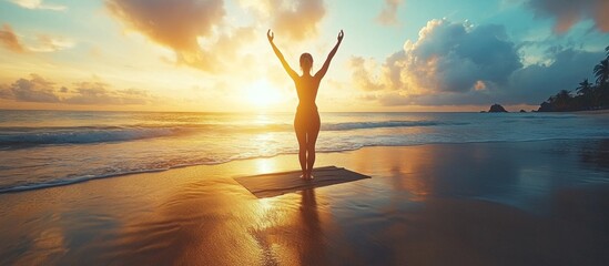 Silhouette of a woman practicing yoga on a sandy beach at sunset.