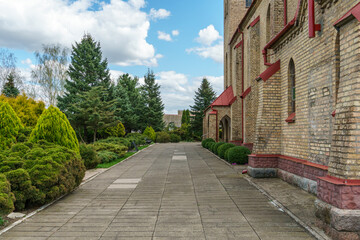 The exterior of the old Gothic red brick church. Arched arches and windows. Green spaces around the church.